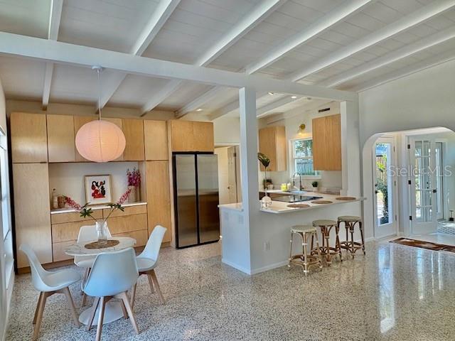 kitchen with lofted ceiling with beams, stainless steel fridge, sink, and light brown cabinets