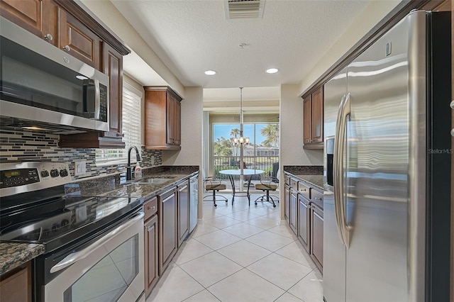 kitchen with backsplash, stainless steel appliances, sink, light tile patterned floors, and a notable chandelier