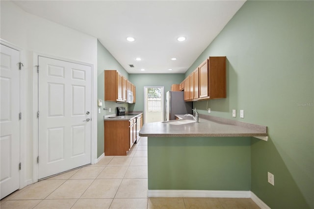 kitchen with kitchen peninsula, sink, light tile patterned floors, and stainless steel appliances