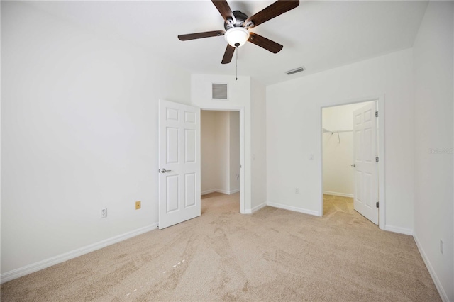 unfurnished bedroom featuring a walk in closet, ceiling fan, a closet, and light carpet