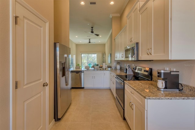 kitchen with appliances with stainless steel finishes, sink, white cabinets, ceiling fan, and light stone counters