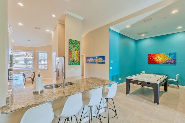 kitchen with sink, hanging light fixtures, light stone counters, ornamental molding, and light tile patterned flooring