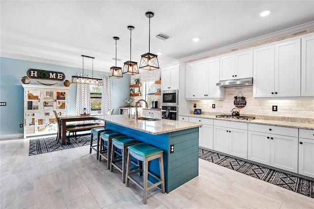 kitchen with appliances with stainless steel finishes, white cabinetry, visible vents, and an island with sink