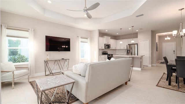 tiled living room featuring a raised ceiling, sink, and ceiling fan with notable chandelier