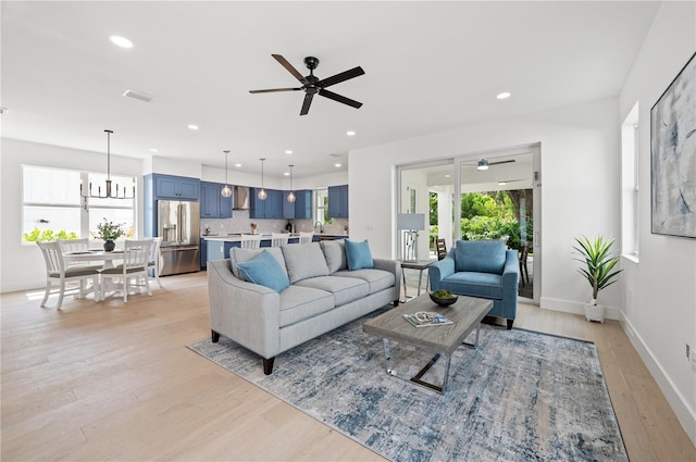 living room featuring ceiling fan with notable chandelier and light wood-type flooring