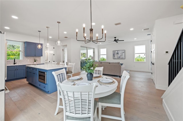 dining room with plenty of natural light, ceiling fan with notable chandelier, and light hardwood / wood-style flooring