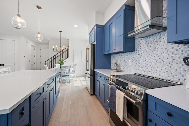 kitchen featuring blue cabinetry, wall chimney exhaust hood, light hardwood / wood-style flooring, a notable chandelier, and high end appliances