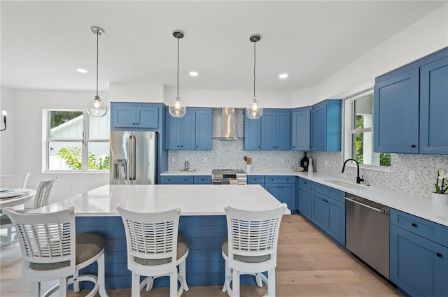 kitchen featuring sink, wall chimney exhaust hood, premium appliances, decorative backsplash, and light wood-type flooring