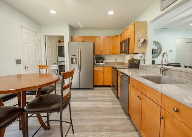 kitchen featuring sink, light stone countertops, light wood-type flooring, stacked washer / drying machine, and stainless steel appliances