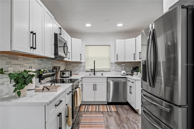 kitchen featuring light stone countertops, white cabinetry, sink, stainless steel appliances, and light wood-type flooring