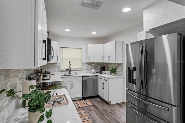 kitchen featuring tasteful backsplash, stainless steel appliances, sink, light hardwood / wood-style floors, and white cabinetry