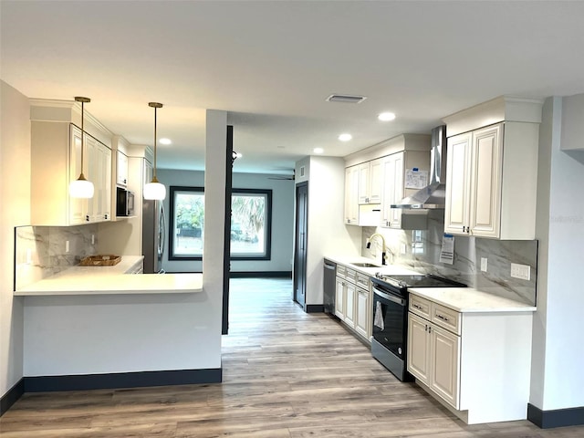 kitchen with wall chimney range hood, sink, decorative light fixtures, white cabinetry, and stainless steel appliances