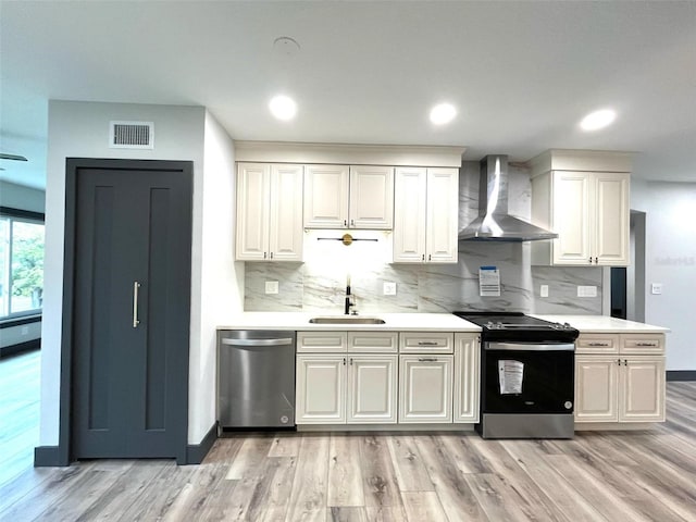 kitchen with wall chimney exhaust hood, appliances with stainless steel finishes, and light hardwood / wood-style flooring