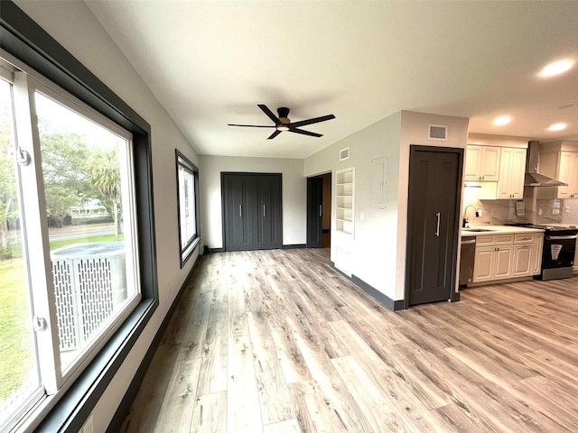 kitchen with white cabinetry, sink, wall chimney range hood, appliances with stainless steel finishes, and light wood-type flooring