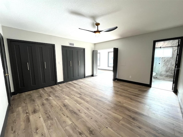 unfurnished bedroom with connected bathroom, light hardwood / wood-style flooring, ceiling fan, and multiple closets