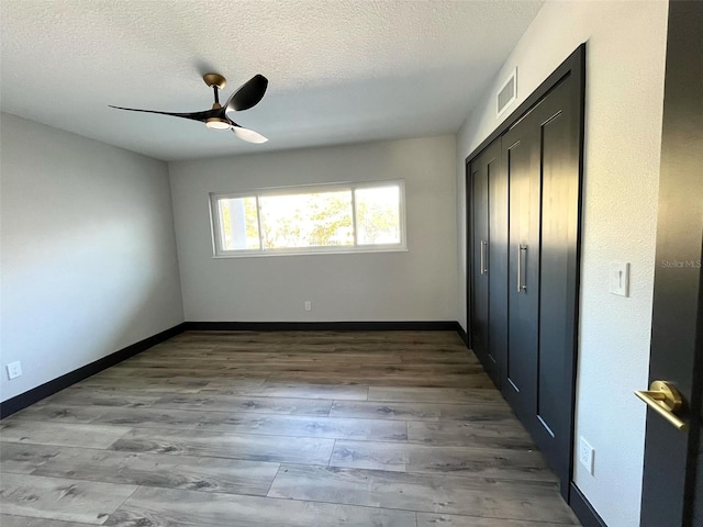 unfurnished bedroom with ceiling fan, a closet, light hardwood / wood-style floors, and a textured ceiling