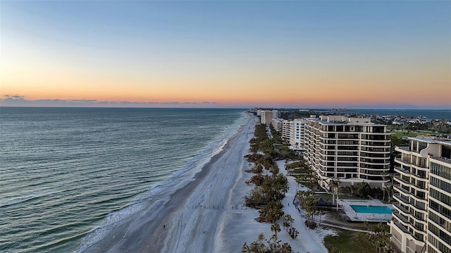 aerial view at dusk featuring a view of the beach and a water view