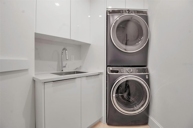 clothes washing area with cabinets, sink, and stacked washing maching and dryer