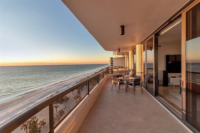 balcony at dusk featuring a view of the beach and a water view