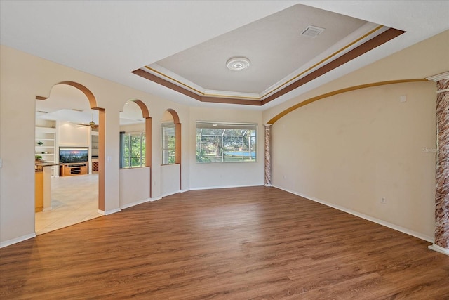 interior space with wood-type flooring, built in shelves, a raised ceiling, ceiling fan, and crown molding