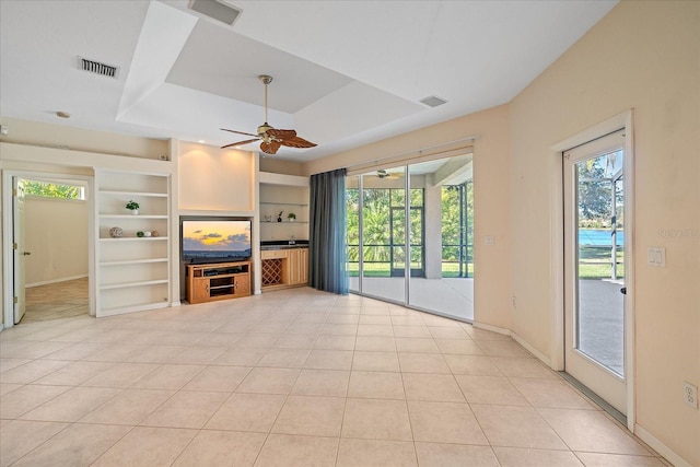 unfurnished living room featuring ceiling fan, light tile patterned floors, a raised ceiling, and built in shelves