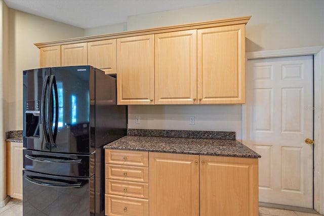 kitchen featuring light tile patterned floors, black fridge with ice dispenser, dark stone counters, and light brown cabinets