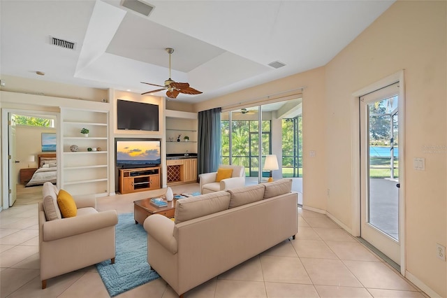 tiled living room with ceiling fan, built in features, and a raised ceiling