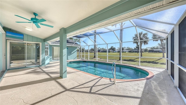 view of swimming pool with glass enclosure, ceiling fan, a patio area, and a lawn