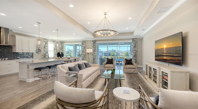 living room featuring ornamental molding, a tray ceiling, light hardwood / wood-style flooring, and a notable chandelier