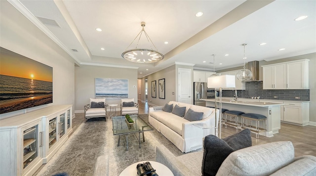 living room featuring a raised ceiling, a notable chandelier, and sink