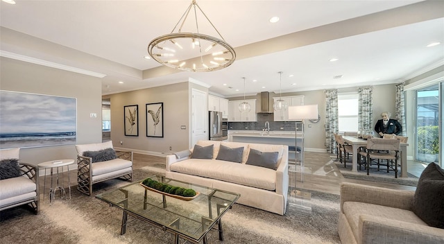 living room with crown molding, sink, a tray ceiling, and an inviting chandelier