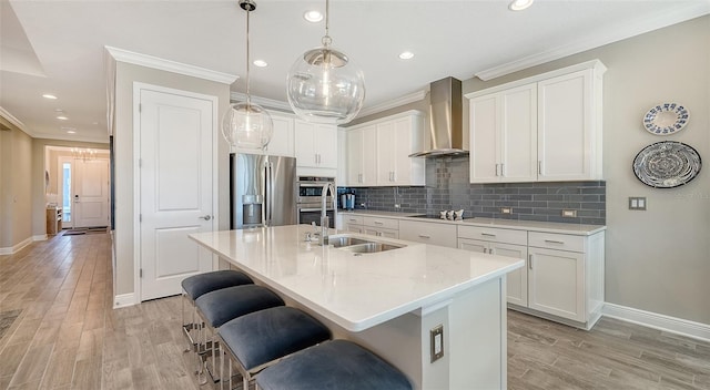 kitchen with white cabinets, a center island with sink, wall chimney exhaust hood, and appliances with stainless steel finishes