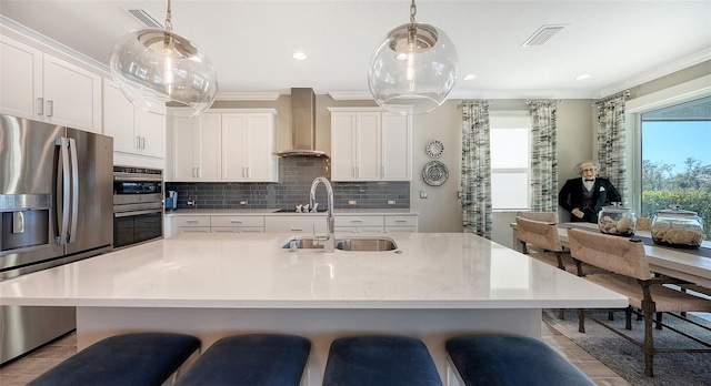 kitchen with white cabinetry, wall chimney range hood, hanging light fixtures, and appliances with stainless steel finishes