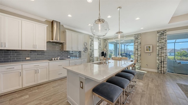 kitchen featuring white cabinetry, sink, wall chimney exhaust hood, decorative light fixtures, and a kitchen island with sink