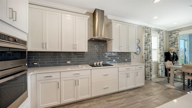 kitchen featuring light hardwood / wood-style floors, wall chimney exhaust hood, white cabinetry, and stainless steel double oven