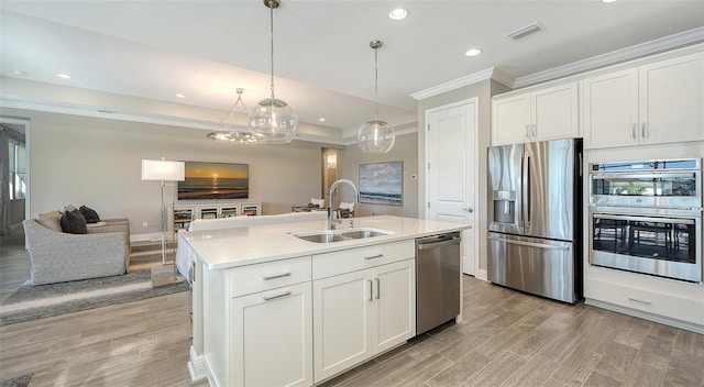 kitchen with white cabinetry, sink, stainless steel appliances, decorative light fixtures, and a center island with sink