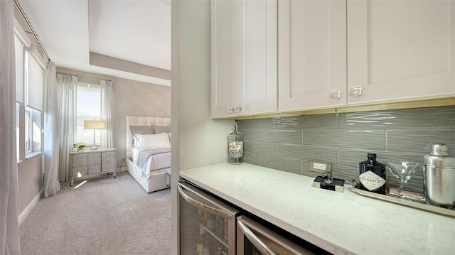 interior space with white cabinets, light colored carpet, wine cooler, a tray ceiling, and light stone counters