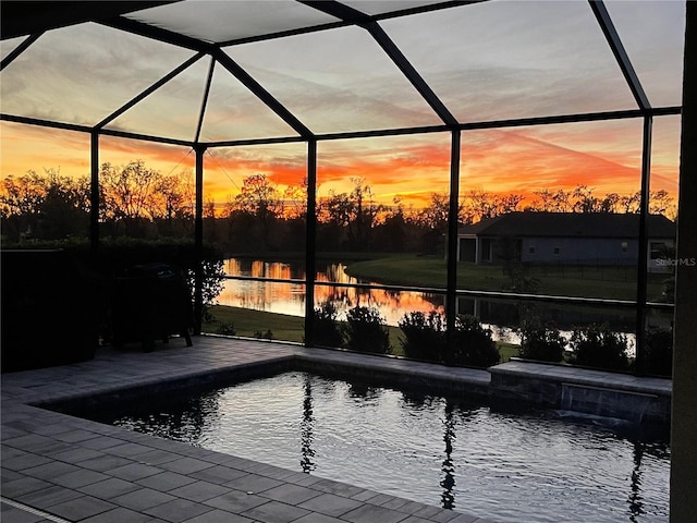 pool at dusk featuring pool water feature, glass enclosure, a patio area, and a water view