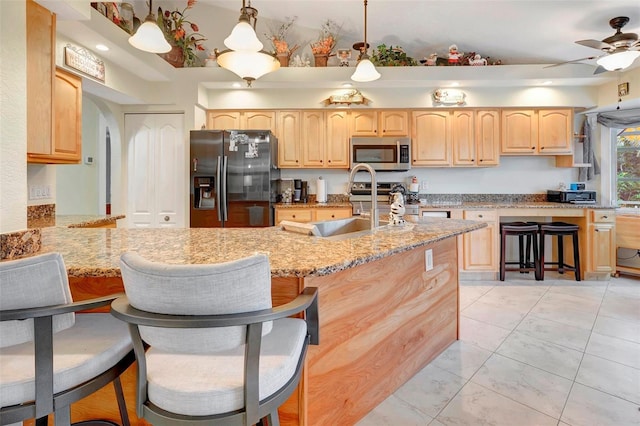 kitchen featuring light stone countertops, light brown cabinetry, stainless steel appliances, and hanging light fixtures