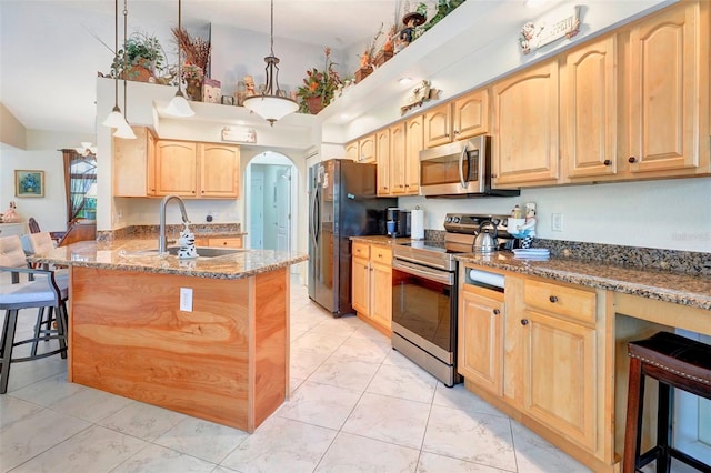 kitchen with a kitchen breakfast bar, sink, dark stone countertops, appliances with stainless steel finishes, and decorative light fixtures