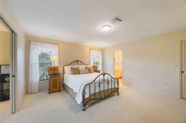 bedroom with light colored carpet, a textured ceiling, and connected bathroom