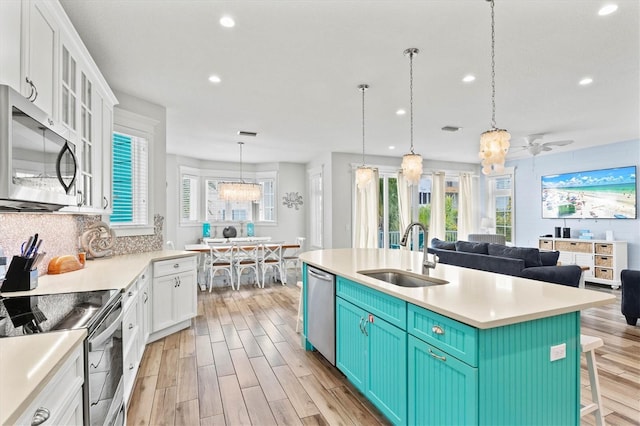 kitchen with sink, stainless steel appliances, a kitchen breakfast bar, a center island with sink, and ceiling fan with notable chandelier