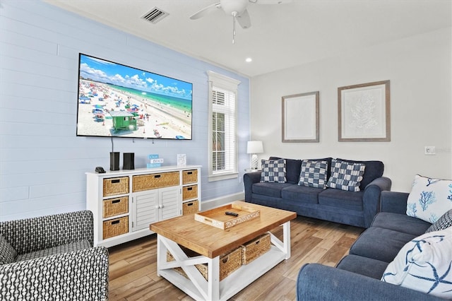 living room featuring light hardwood / wood-style flooring, ceiling fan, and wooden walls