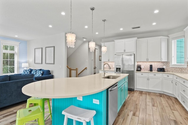 kitchen with sink, an island with sink, decorative light fixtures, white cabinets, and appliances with stainless steel finishes