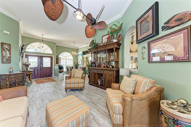 living room with a notable chandelier, light wood-type flooring, ornamental molding, and french doors