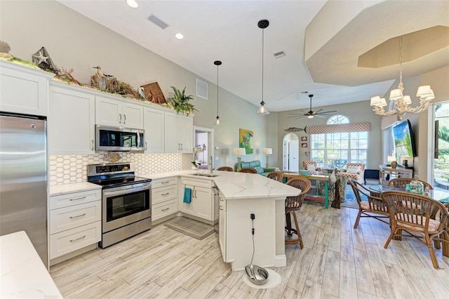 kitchen with ceiling fan with notable chandelier, stainless steel appliances, hanging light fixtures, and light hardwood / wood-style floors