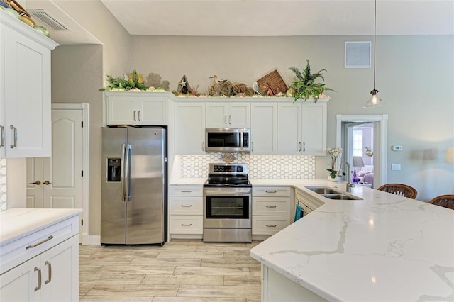 kitchen with appliances with stainless steel finishes, light wood-type flooring, sink, decorative light fixtures, and white cabinetry