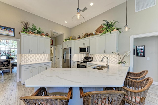 kitchen with sink, kitchen peninsula, light hardwood / wood-style floors, decorative light fixtures, and appliances with stainless steel finishes