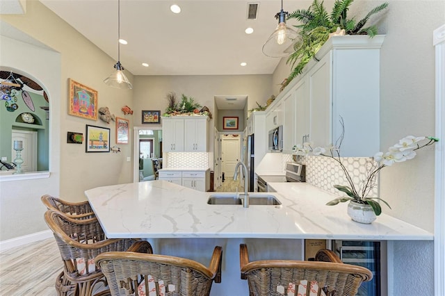 kitchen with appliances with stainless steel finishes, light stone counters, sink, decorative light fixtures, and white cabinetry