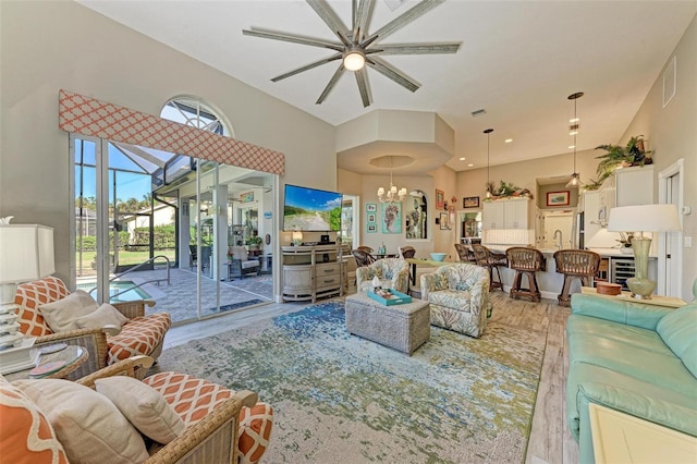 living room with sink, a towering ceiling, light hardwood / wood-style floors, and ceiling fan with notable chandelier